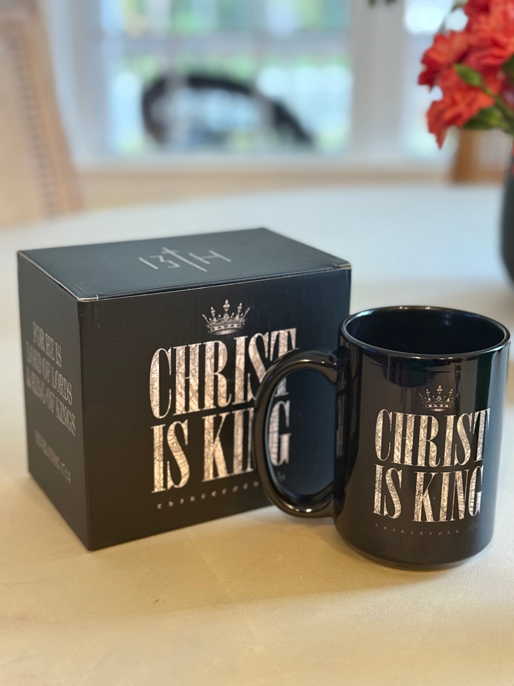 The Christ is King Mug by 13th, with bold white lettering and a crown above, comes in a matching box—both displayed on a light surface.