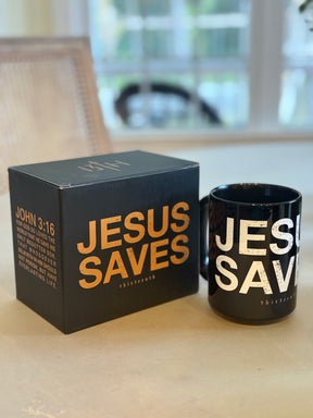 The 13th Jesus Saves Mug and its matching box display bold gold and white "JESUS SAVES" text, with John 3:16 in gold on the box. Both are shown on a light table with a window behind them.