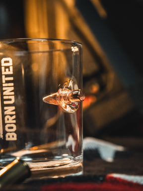 The Born United Bullet Whiskey Glass by Born United Private Label features a real bullet embedded in the side and "BORN UNITED" printed vertically, making it a distinctive and memorable addition to any bar collection.