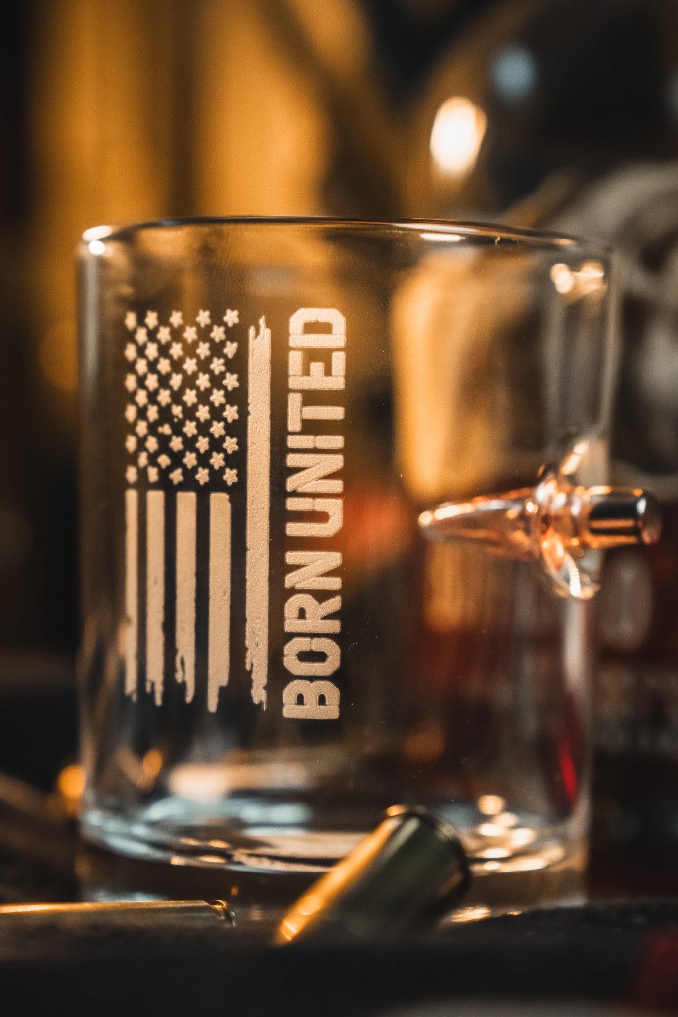 The Born United Bullet Whiskey Glass by Born United Private Label features a clear design with an American flag and "BORN UNITED" print, plus an embedded bullet for a unique touch—perfect for whiskey enthusiasts.