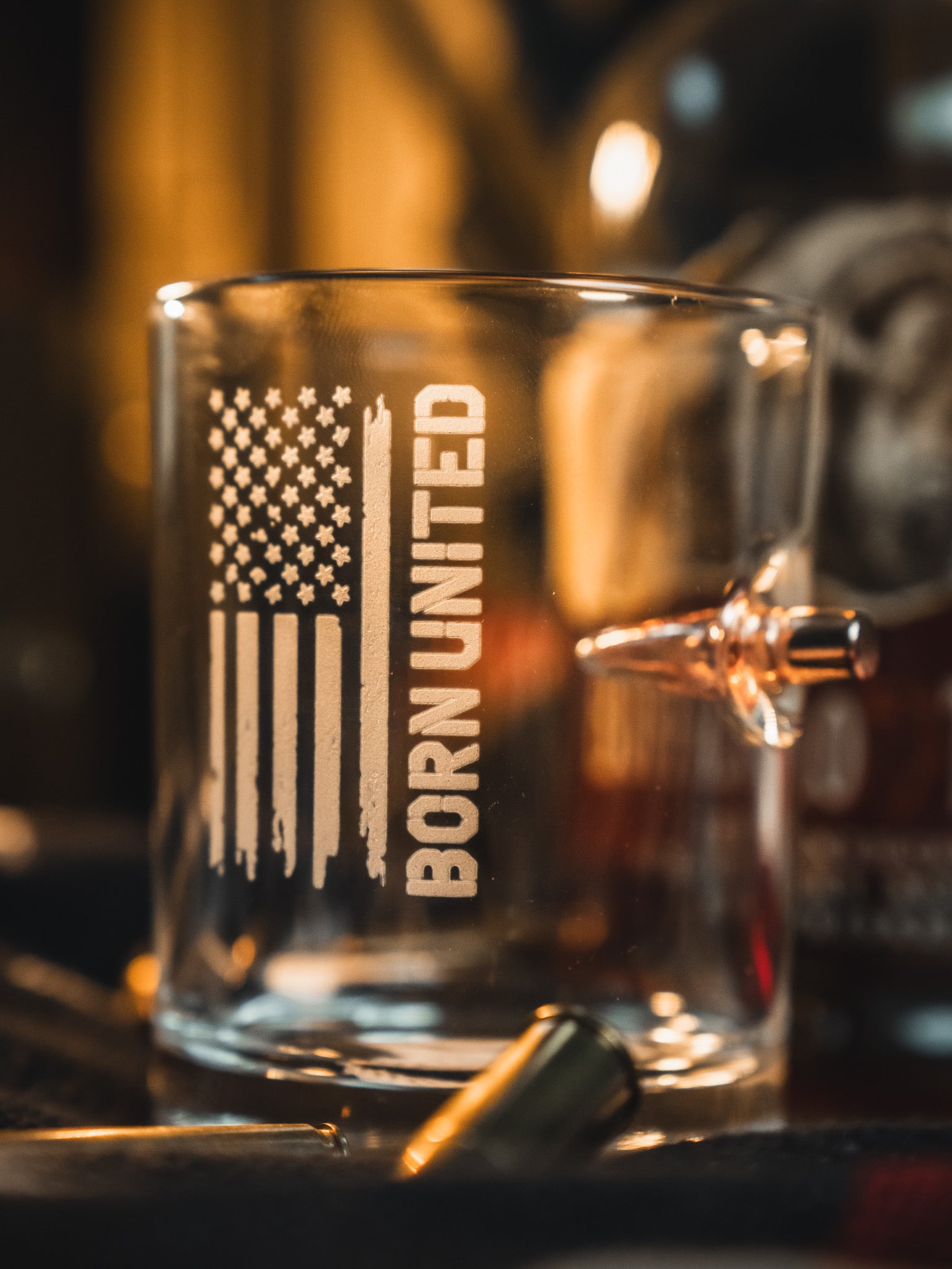 The Born United Bullet Whiskey Glass by Born United Private Label features a clear design with an American flag and "BORN UNITED" print, plus an embedded bullet for a unique touch—perfect for whiskey enthusiasts.