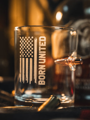 The Born United Bullet Whiskey Glass by Born United Private Label features a clear design with an American flag and "BORN UNITED" print, plus an embedded bullet for a unique touch—perfect for whiskey enthusiasts.
