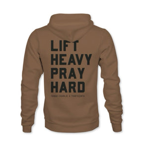 A brown hoodie from Tango Charlie Apparel, featuring "LIFT HEAVY. PRAY HARD." in bold black text on the back, with "TANGO CHARLIE X THIRTEENTH" below. Made from a comfy cotton-poly blend.
