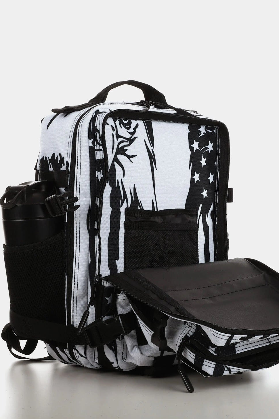 The American Stealth Special Edition Tac-Pac - 25L by Born United Private Label is a black and white backpack with graphic designs, featuring open compartments, side mesh pockets holding a black bottle, and an unzipped front flap revealing the interior against a plain white backdrop.