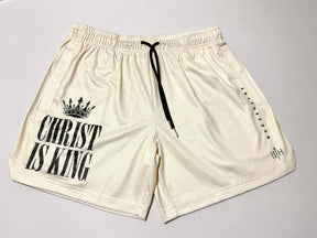 The 13th Men's Mesh Lifestyle Shorts | 5.5" - Christ is King Ivory feature a cream-colored mesh design with "CHRIST IS KING" and a crown graphic printed on the left leg, a black drawstring, and subtle black text on the right leg; these unisex shorts combine comfort and style for everyday wear.