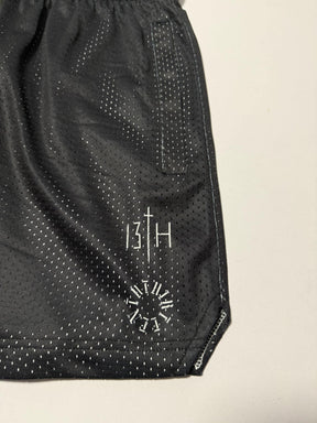 Men's Mesh Lifestyle Shorts | 5.5"- Forgiven by 13th feature a black athletic design with white dotted lines, a vertical pocket, and the signature 13TH logo above a circular Roman numeral detail near the hem. Crafted from breathable mesh fabric, these unisex shorts combine comfort and style for any activity.