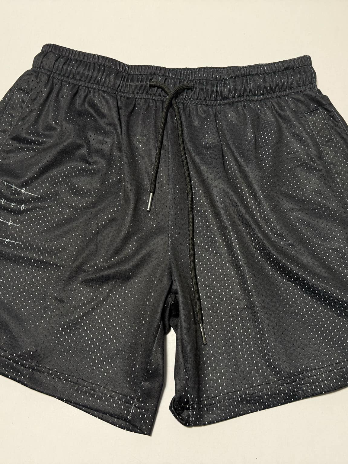 The 13th Men's Mesh Lifestyle Shorts | 5.5" - Forgiven, featuring an elastic waistband, black drawstring, and side pockets, are classic unisex black shorts designed for all-day comfort and style—shown here laid flat on a light surface.