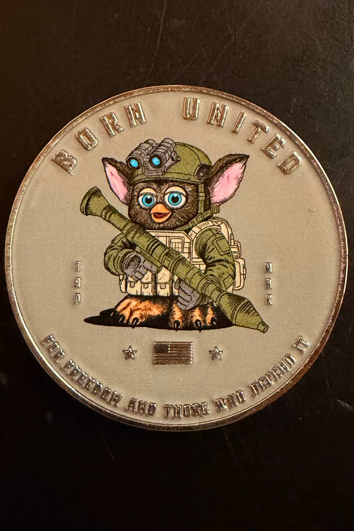 The Furbinator Challenge Coin by Born United Private Label features a cartoon Furbinator like Gizmo in military gear with night-vision goggles and a rocket launcher, plus the text: BORN UNITED and FOR FREEDOM AND THOSE WHO DEFEND IT.