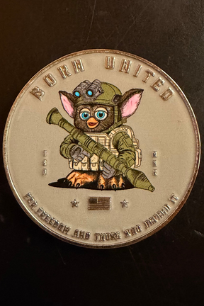 The Furbinator Challenge Coin by Born United Private Label features a cartoon Furbinator like Gizmo in military gear with night-vision goggles and a rocket launcher, plus the text: BORN UNITED and FOR FREEDOM AND THOSE WHO DEFEND IT.