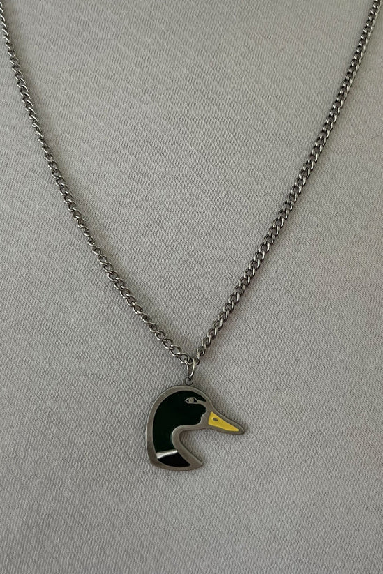 The Mallard OG Stainless Steel Necklace by Mucker Bucket features a pendant of a stylized duck head in green, yellow, and black. Made in the USA for quality craftsmanship, it is displayed on a silver chain against a light gray background.