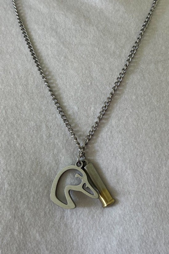 The Mallard Duck Shot necklace from Mucker Bucket showcases a stainless steel pendant with a horse head silhouette and a bullet casing design, beautifully displayed on white fabric. Made in the USA.
