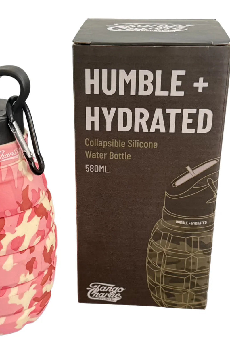 The Pink Camo Humble + Hydrated 20oz Water Bottle by Tango Charlie Apparel features BPA-free, food-grade silicone with a black cap and carabiner, shown beside its box—safe, collapsible, and convenient for hydration on the go.