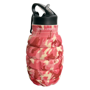 The Tango Charlie Apparel Pink Camo Humble + Hydrated 20oz Water Bottle features a pink, red, and beige camo design with a black cap and carabiner. Made from BPA-free, food-grade silicone, it has "HUMBLE + HYDRATED" printed near the top.