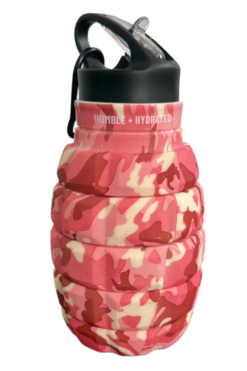 The Tango Charlie Apparel Pink Camo Humble + Hydrated 20oz Water Bottle features a pink, red, and beige camo design with a black cap and carabiner. Made from BPA-free, food-grade silicone, it has "HUMBLE + HYDRATED" printed near the top.