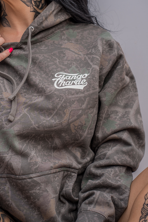 Sporting the “Lift Heavy. Trust God.” Premium Darkwood Camo Hoodie from Tango Charlie Apparel, this individual showcases both style and strength, complemented by visible neck and hand tattoos—including a subtle nod to Christian fitness—that reflect the spirit of Proverbs 3:5-6.