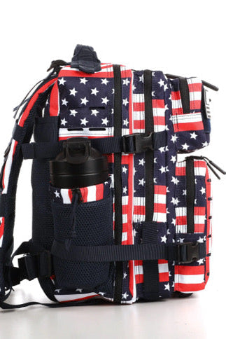The Ultimate Patriot Special Edition Tac-Pac - 25L by Born United Private Label features an American flag design with stars and stripes, includes multiple compartments with a side pocket for a black bottle, and contrast straps and zippers on a pristine white background.