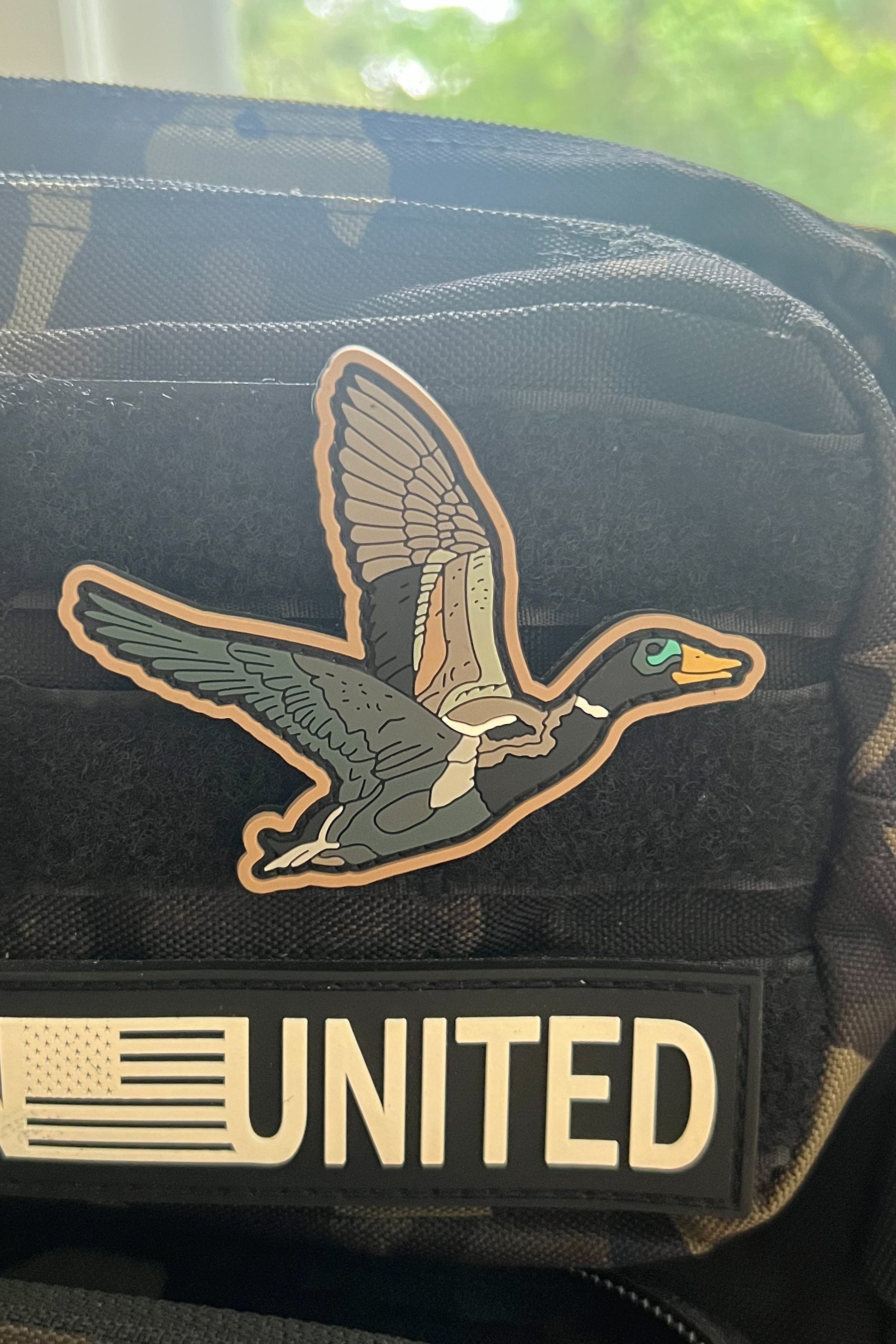 Black tactical vest with a duck patch and 'Born United' text on a blurred background