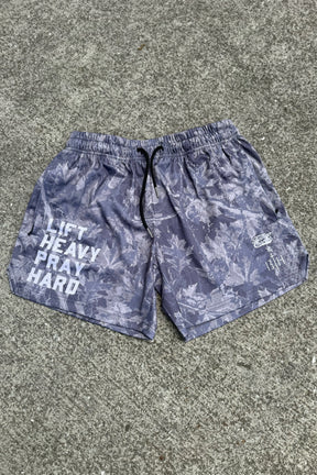 The Men's Mesh Lifestyle Shorts | 5.5" - Lift Heavy Pray Hard Deadwood by Tango Charlie Apparel feature a gray leaf pattern, black drawstring, bold "LIFT HEAVY PRAY HARD" text on the left leg, and white graphics on the right—ideal for active men.