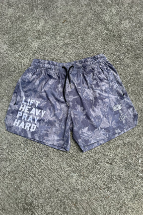 Tango Charlie Apparel Men's Mesh Lifestyle Shorts | 5.5" - Lift Heavy Pray Hard Deadwood, gray with leaf pattern and “LIFT HEAVY PRAY HARD” in bold white on the left leg, displayed on a concrete surface.