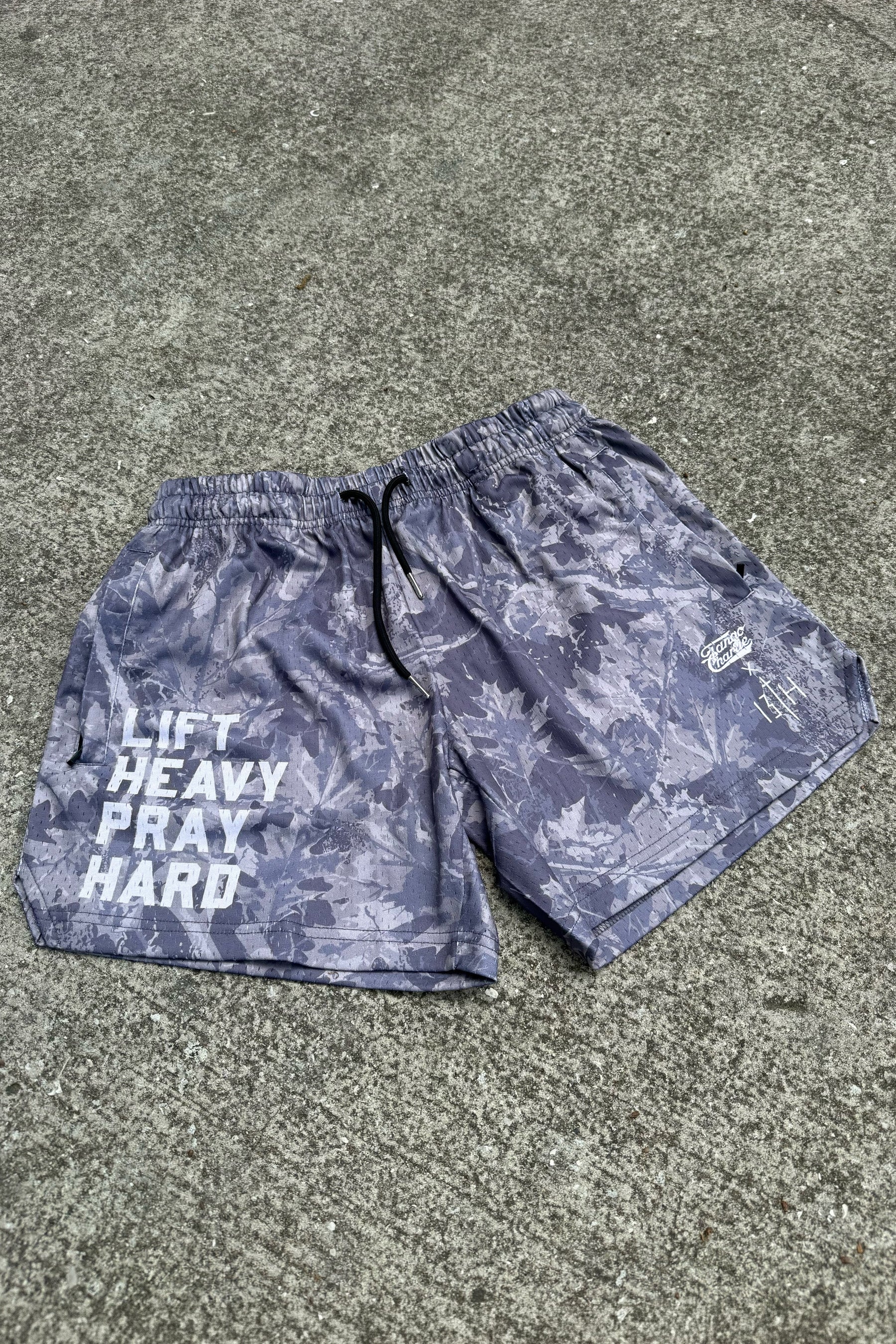 The Men's Mesh Lifestyle Shorts | 5.5" - Lift Heavy Pray Hard Deadwood by Tango Charlie Apparel feature gray camo with white text and graphics on the right leg—perfect for the gym or your active lifestyle.