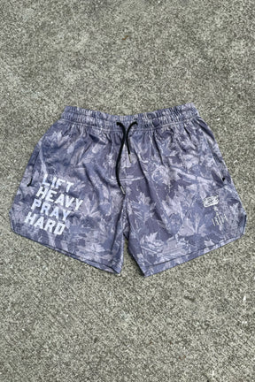 The Tango Charlie Apparel Men's Mesh Lifestyle Shorts (5.5") in gray feature a leaf pattern, "LIFT HEAVY PRAY HARD" text on the left leg, and a small logo on the right leg, shown lying flat on concrete.