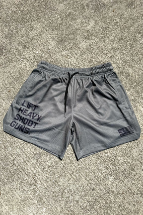 Tango Charlie Apparel's Men's Mesh Lifestyle Shorts in OD Green with a 5.5" inseam feature "LIFT HEAVY, SHOOT GUNS" on the left leg and a small NOBLE UNITED logo on the right, displayed on a concrete surface.