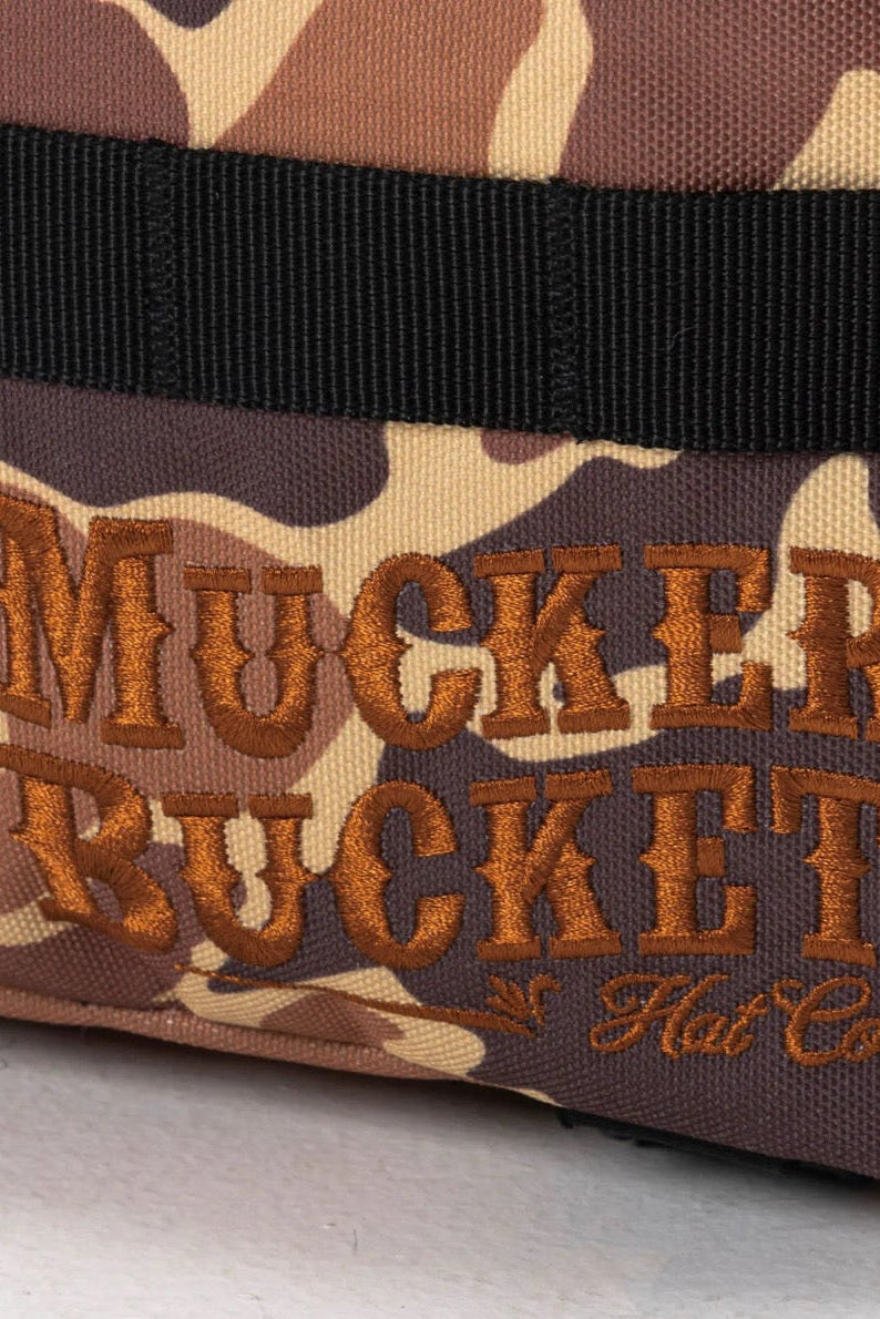 A close-up of the Duck It Limited Edition Tac-Pac - 25L by Mucker Bucket, featuring brown and tan camouflage with bold orange embroidery—an ideal hunting backpack.