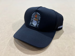 The Born United Premium Snapback - Burning Bridges by Born United Private Label features a black design with a burning torch patch and "May the bridges I burn light my way" embroidered on the front, plus a side label. Displayed on a beige surface.