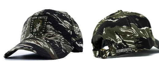 Two Born United Private Label Buckle Hats—Savage Operations edition—are shown, one front and one back. Both have a black and green camo pattern; the front displays a Born United patch, the back shows the brand name above an adjustable strap.