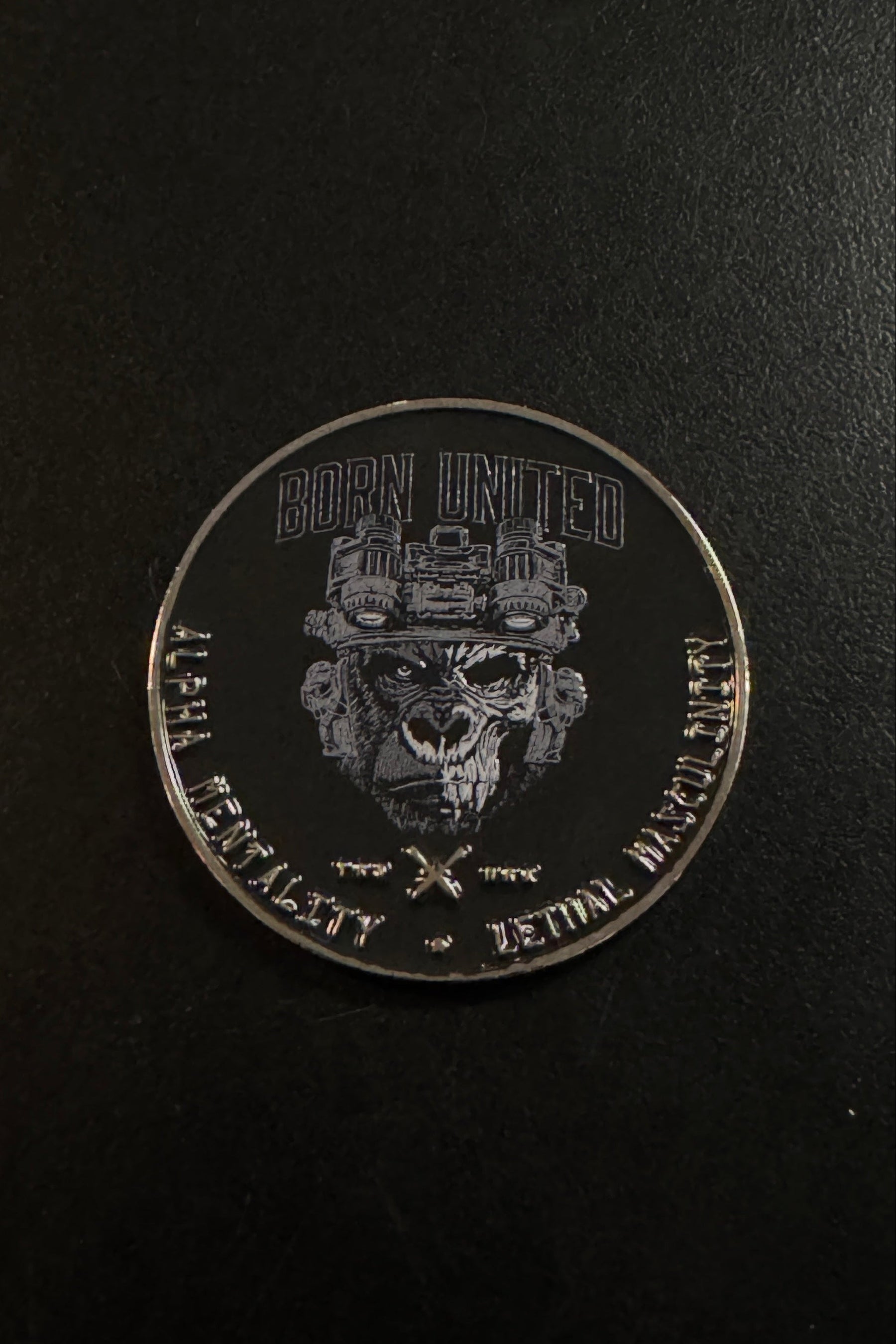 A round silver challenge coin featuring a military skull emblem and the text 'BORN UNITED' and 'DEADLY VALUABLE - BORN TO WIN' on a dark background.