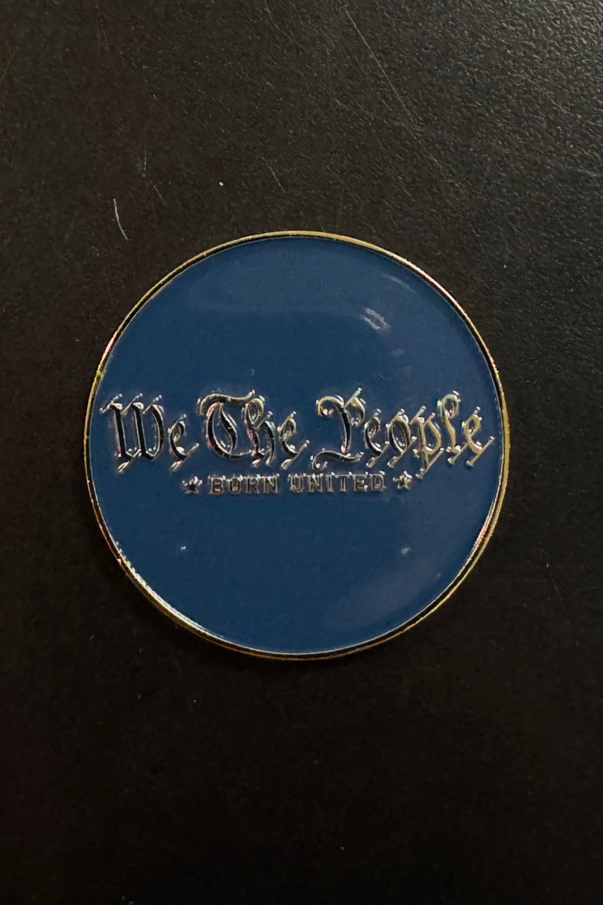 Certainly! Here’s a rewritten sentence using the provided product data: The Born United Private Label “We The People Challenge Coin” features a round blue design with gold trim and showcases the words “We The People” and “Born United” in silver gothic-style lettering, evoking the look of a classic challenge coin.
