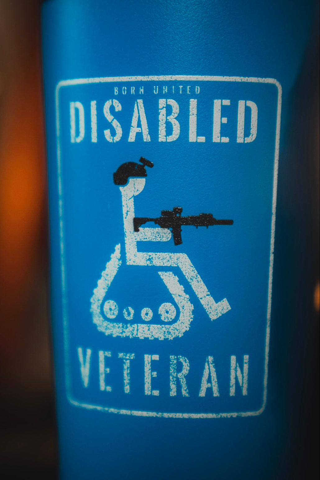 A blue sign features a wheelchair with tank tracks and a person holding a rifle, labeled “Born United Disabled Veteran”—a powerful design for the 20oz Disabled Veteran Tumbler from Born United Private Label.