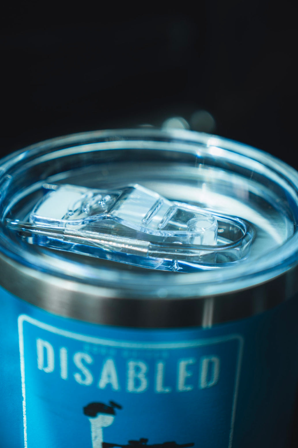 A close-up of the Born United Private Label Disabled Veteran Tumbler - 20oz in blue stainless steel with a clear plastic lid, cupholder approved, featuring a partially visible "DISABLED" sign.