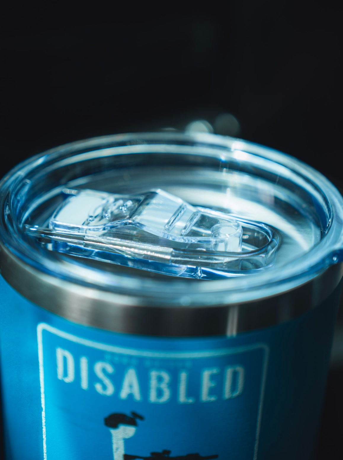 A close-up of the Born United Private Label Disabled Veteran Tumbler - 20oz in blue stainless steel with a clear plastic lid, cupholder approved, featuring a partially visible "DISABLED" sign.
