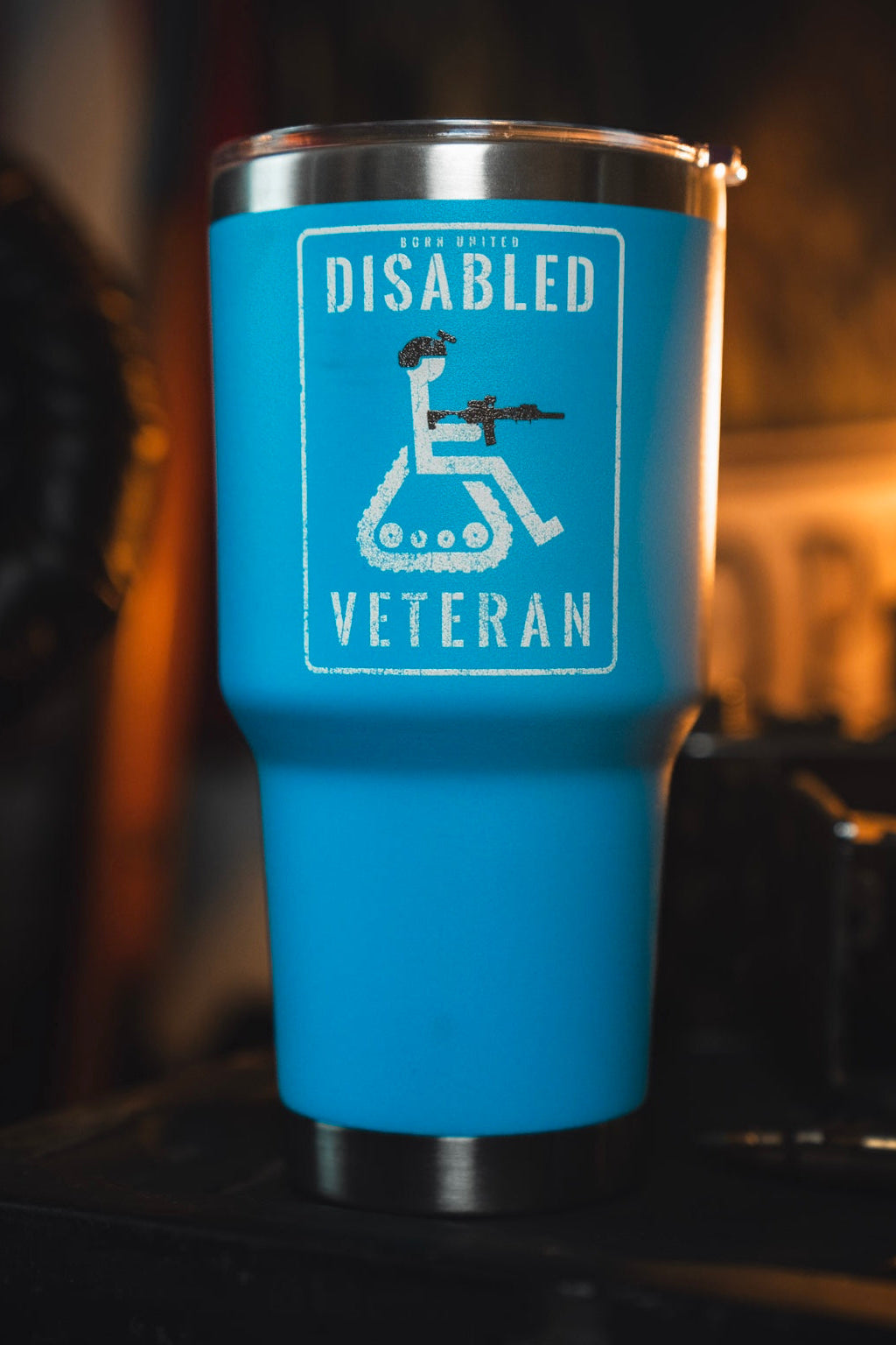 The Disabled Veteran Tumbler - 30oz by Born United Private Label features a blue design with a stylized wheelchair, military helmet, and rifle set against a blurred background.