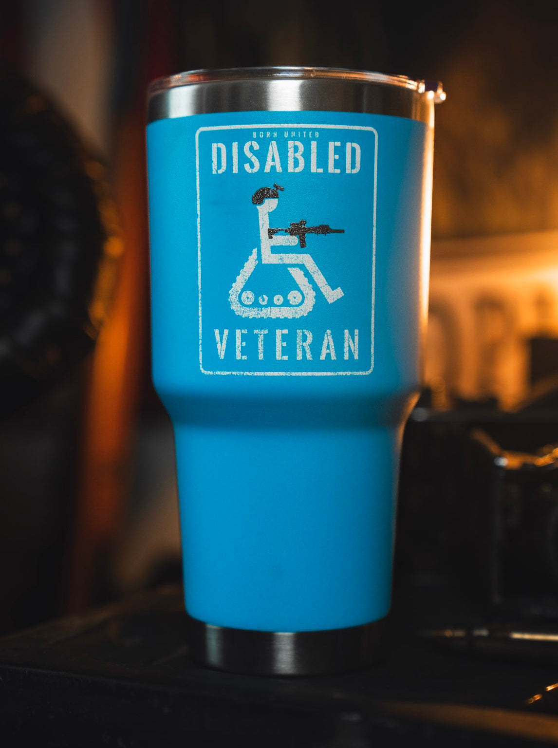 The Disabled Veteran Tumbler - 30oz by Born United Private Label features a blue design with a stylized wheelchair, military helmet, and rifle set against a blurred background.