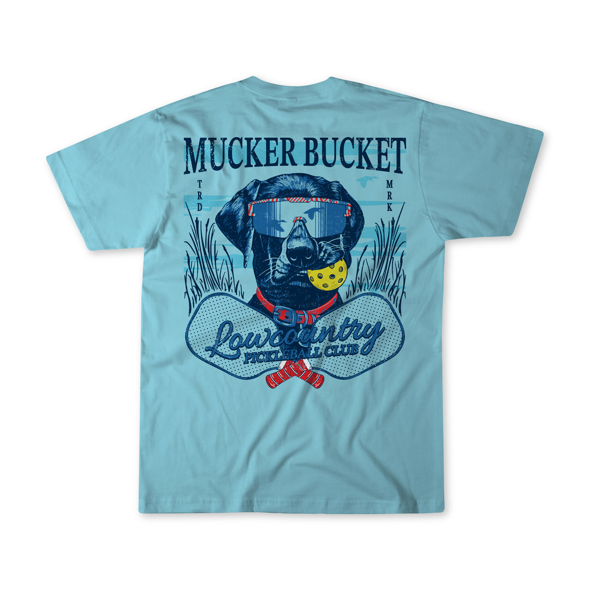 The Youth Pickleball Retriever Premium Tee by Mucker Bucket is a light blue shirt with a dog in goggles holding a yellow ball among grass and paddles. Mucker Bucket appears above and Lowcountry Beach Club below the graphic.