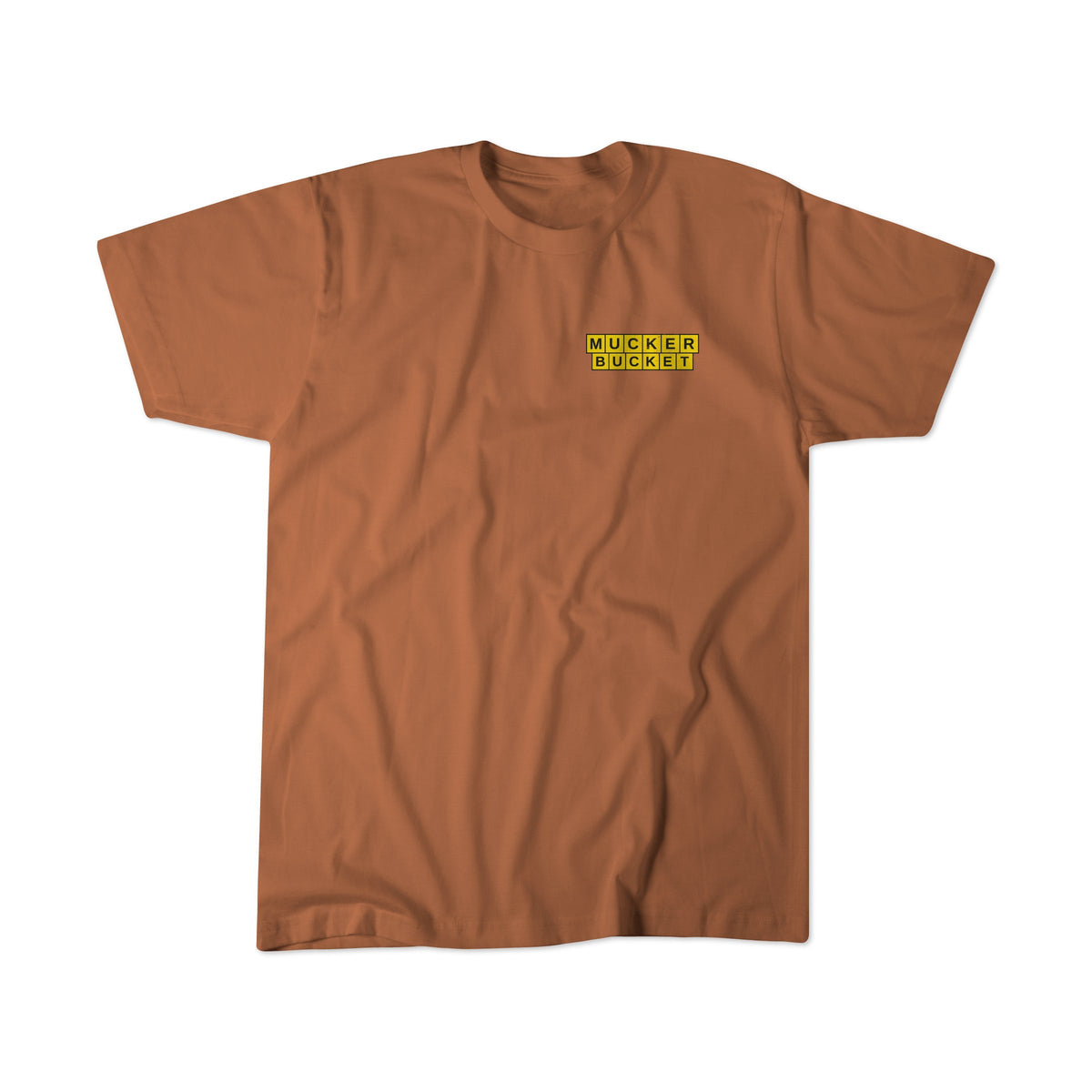 The Mucker Bucket American Tradition Premium Tee is a brown relaxed fit shirt with a yellow and black "MUCKER BUCKET" patch on the left chest, shown laid flat on a white background.