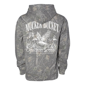 The Mucker Bucket Mallard Deadwood Camo Hoodie is a stylish fleece with a relaxed fit, showcasing a bold white flying ducks and reeds graphic plus Mucker Bucket Southern Goods OFFICIAL TRADEMARK on the back.