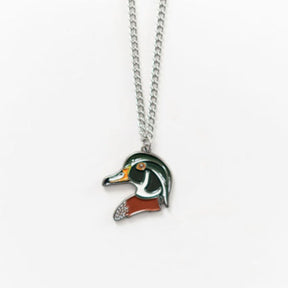 The Mucker Bucket Wood Duck Necklace features a ducks head pendant in vibrant green, orange, and white on a simple stainless steel chain with a white backdrop. Made in the USA, it exudes elegance and charm.