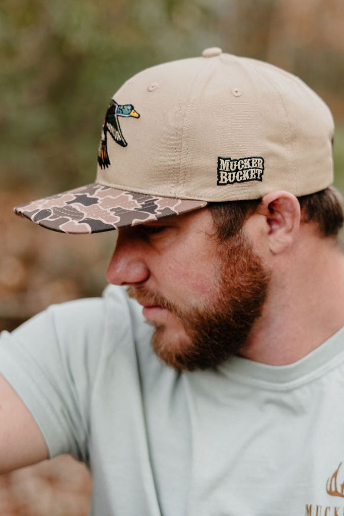 Man wearing a beige cap with a logo and text, outdoors.