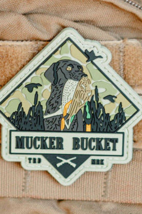 Patch with a dog and owl design on a beige background, featuring the text 'Mucker Bucket'.