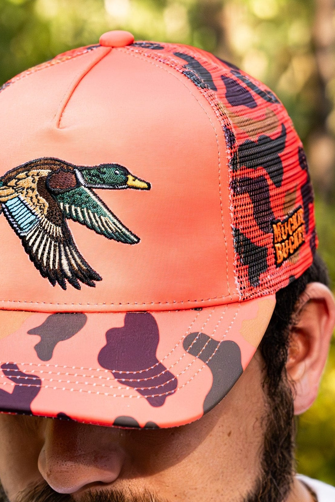 Coral and black camouflage cap with duck design worn by a person outdoors