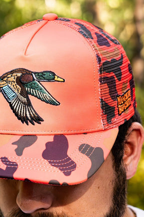 Coral and black camouflage cap with duck design worn by a person outdoors