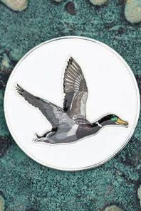 The OG Duck Lucky Huntin Coin pin by Mucker Bucket features a mallard duck in flight, detailed against a white background with realistic colors on a textured green surface, making it a must-have for collectors.