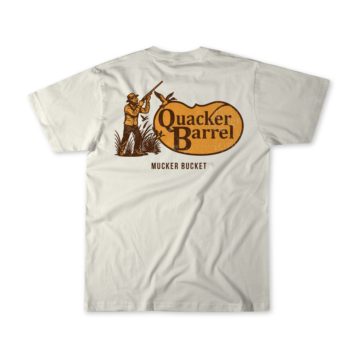 The Quacker Barrel Premium Tee by Mucker Bucket is cream-colored ring-spun cotton, featuring a bold back graphic of a hunter, brown grass, and an orange sign with “MUCKER BUCKET” printed below.