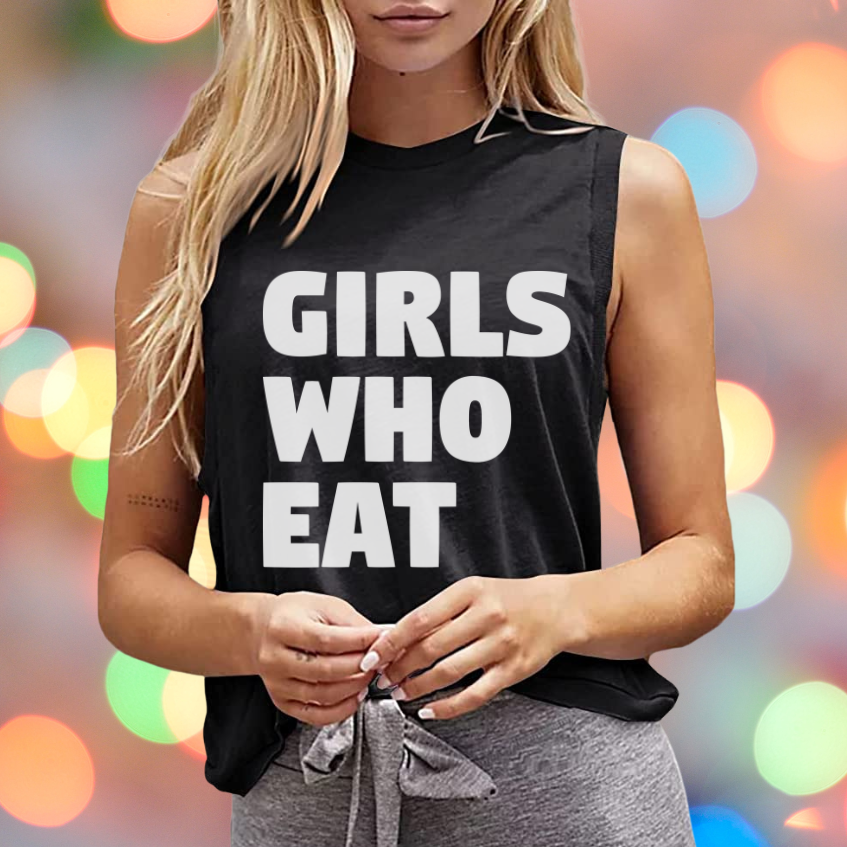 A woman with long blonde hair wears the "Girls Who Eat Crop Tank" by Tango Charlie Apparel—an inspirational black sleeveless top featuring bold white text, ideal gym wear. The background is colorful and blurred with circular lights.