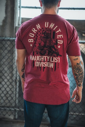 A person stands with their back to the camera, sporting the Born United Private Label Tactical Santa Tee, which features an armed Saint Nick in sunglasses over an American flag and reads "Born United Naughty List Division"—ideal for Christmas cheer.