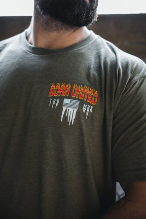 A man wears an olive green Tactical Miser Operations t-shirt by Born United Private Label, featuring “BORN UNITED” in orange flaming letters with white melting lines and text on the left chest.