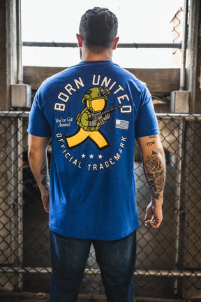 A tattooed man faces away, wearing a blue Born United Private Label "You've Got Ammo!" T-shirt with a cartoon soldier and "Born United Official Trade Mark"—a playful nod to retro tech humor.